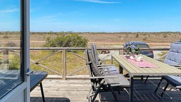 Una terraza de madera con mesa y sillas, un vidrio y vistas al paisaje.