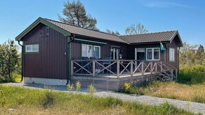 Eine zweistöckige Holzhütte mit einem Balkon, einer Schotterauffahrt und blauem Himmel.