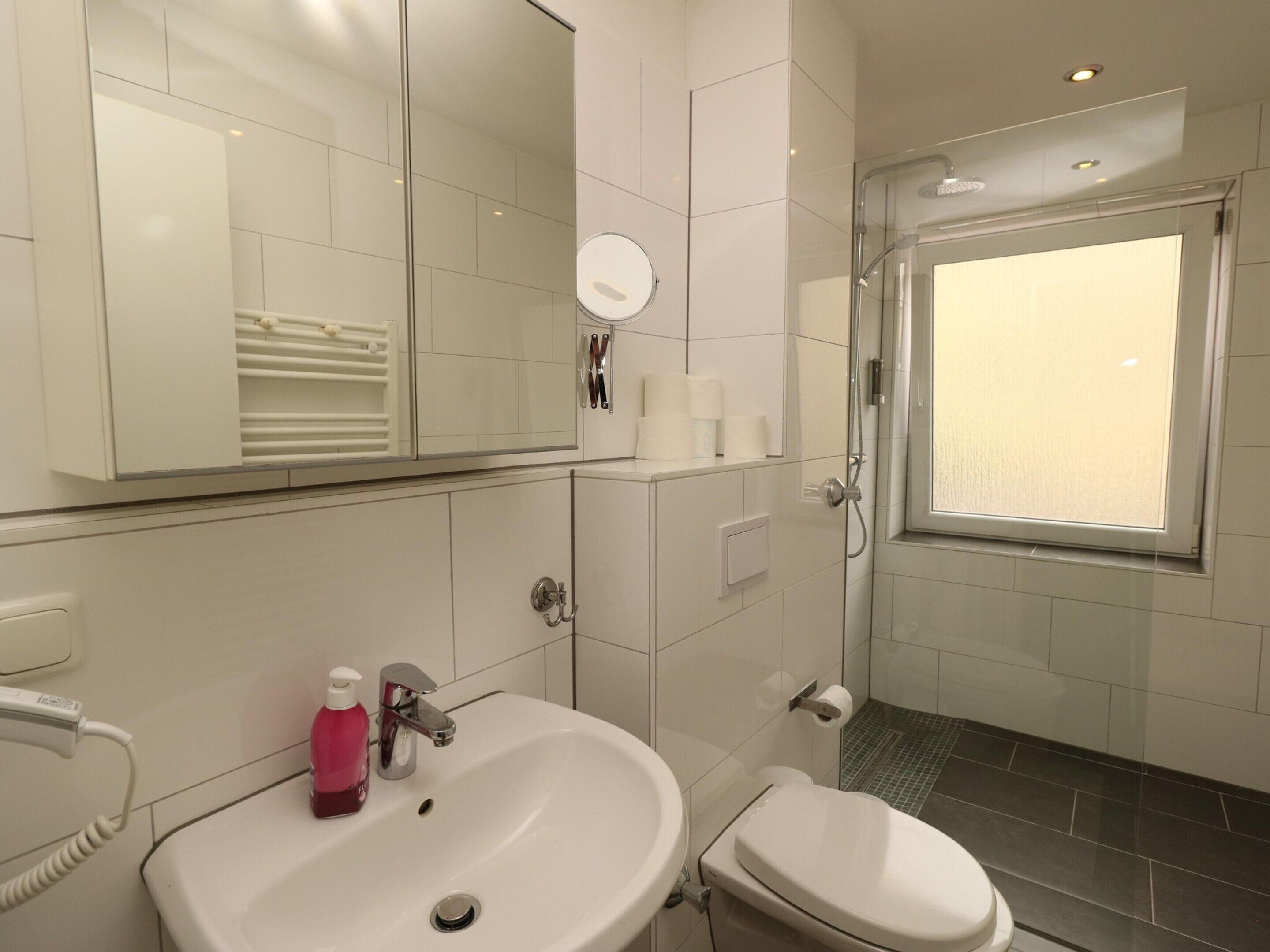 A modern bathroom with a white sink, toilet, and glass shower enclosure.