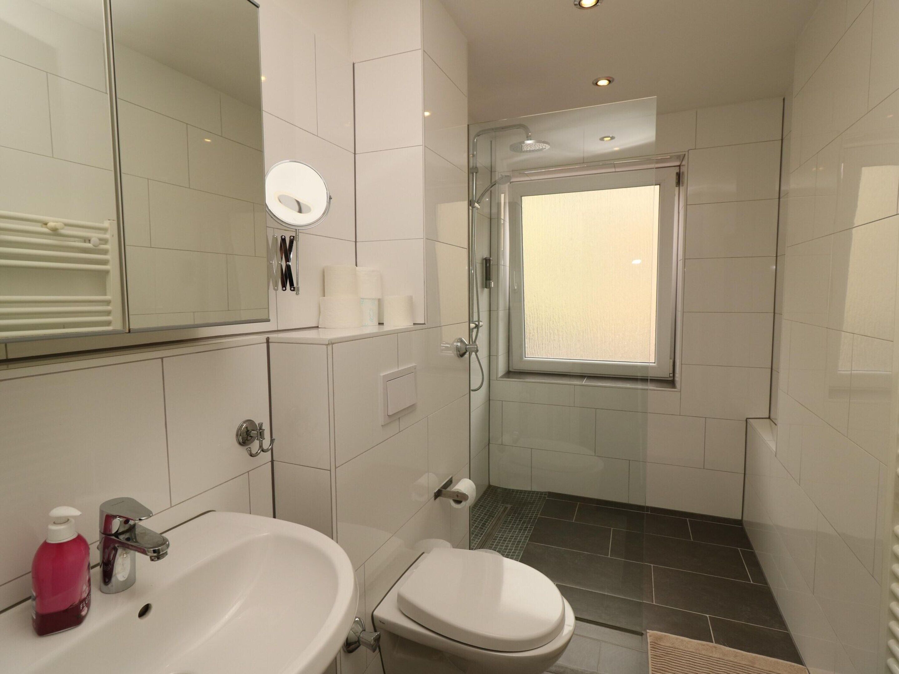 Une salle de bain avec un lavabo blanc, des toilettes, une douche en verre et une fenêtre.