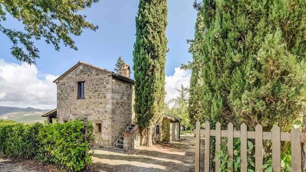 A stone building with a small staircase leading to a door, surrounded by greenery and a wooden fence. - Belvilla by OYO Typical Country House With Pool (San Casciano dei Bagni)