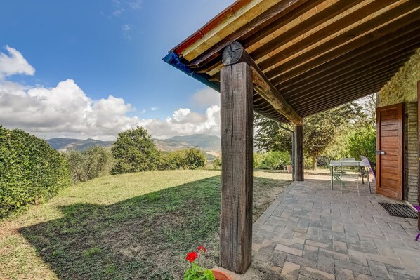 A covered patio area with a view of a grassy landscape and distant mountains. - Belvilla by OYO Typical Country House With Pool (San Casciano dei Bagni)