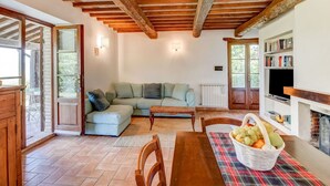 A cozy living room with a sofa, a wooden table with a fruit basket, and a fireplace. - Belvilla by OYO Typical Country House With Pool (San Casciano dei Bagni)