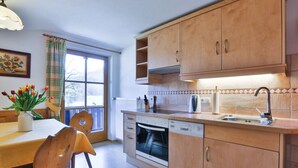 A kitchen with wooden cabinets, a built-in oven, and a window with curtains. - Haus Brandl Modern Retreat (Ramsau bei Berchtesgaden)