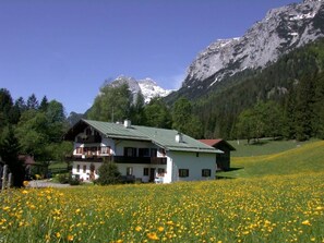 A two-story house with a green roof, surrounded by a field of yellow flowers, with a mountain in the background. - Haus Brandl Modern Retreat (Ramsau bei Berchtesgaden)