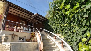 Una escalera de piedra conduce a una terraza de madera con mobiliario exterior, rodeada por un denso seto verde.
