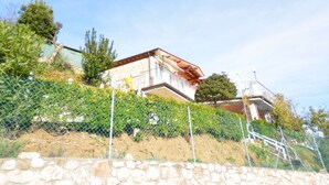 Un edificio de piedra con techo inclinado, rodeado por una cerca de alambre y follaje.