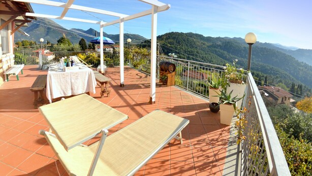 Una terraza con mesa lista para comer, sillas de descanso y vistas a las montañas.