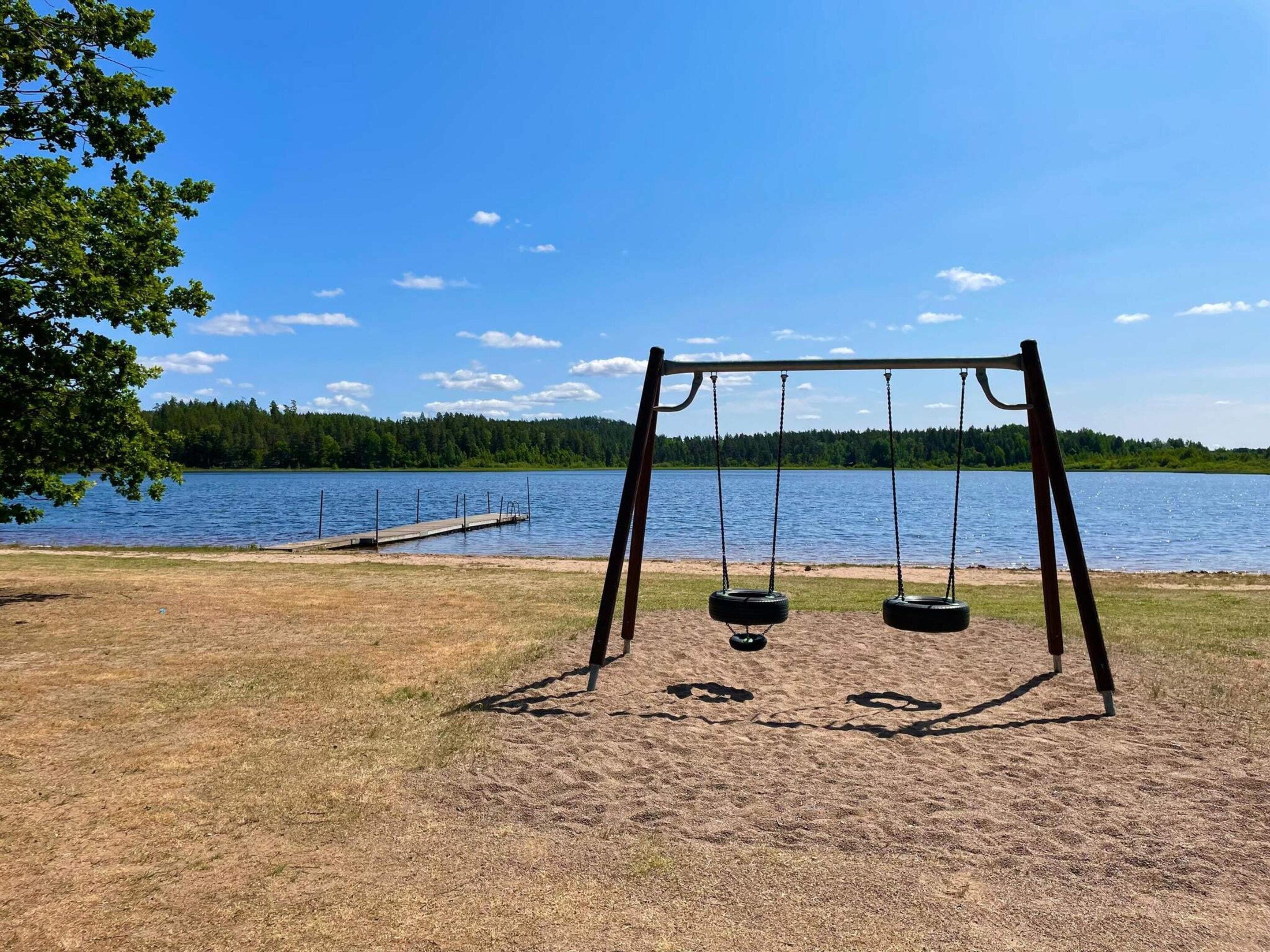 A swing set by a lake with a dock in the background.
