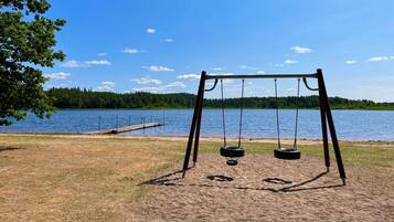A swing set by a lake with a dock in the background.