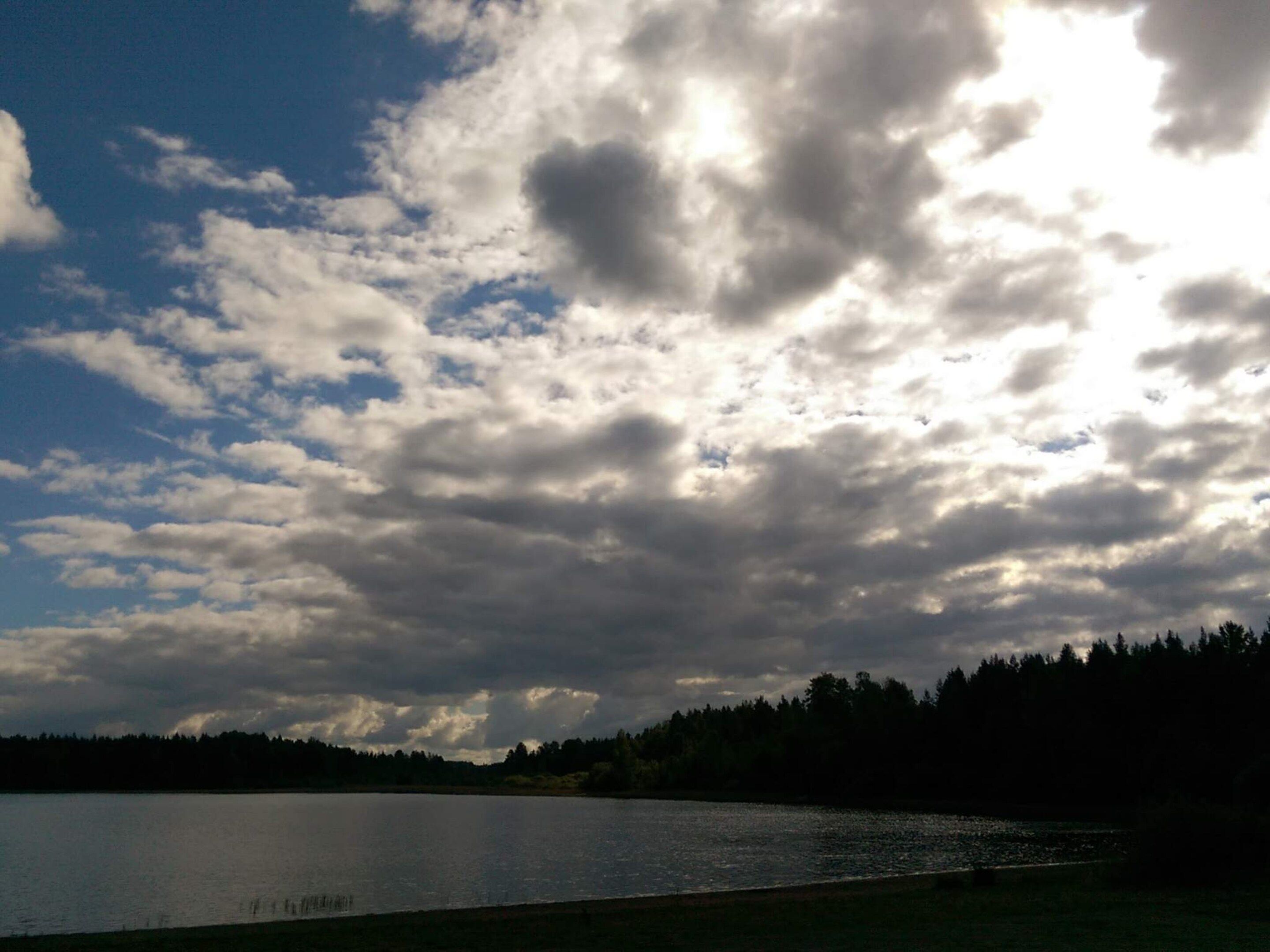 A lake with a forested shoreline and a cloudy sky.