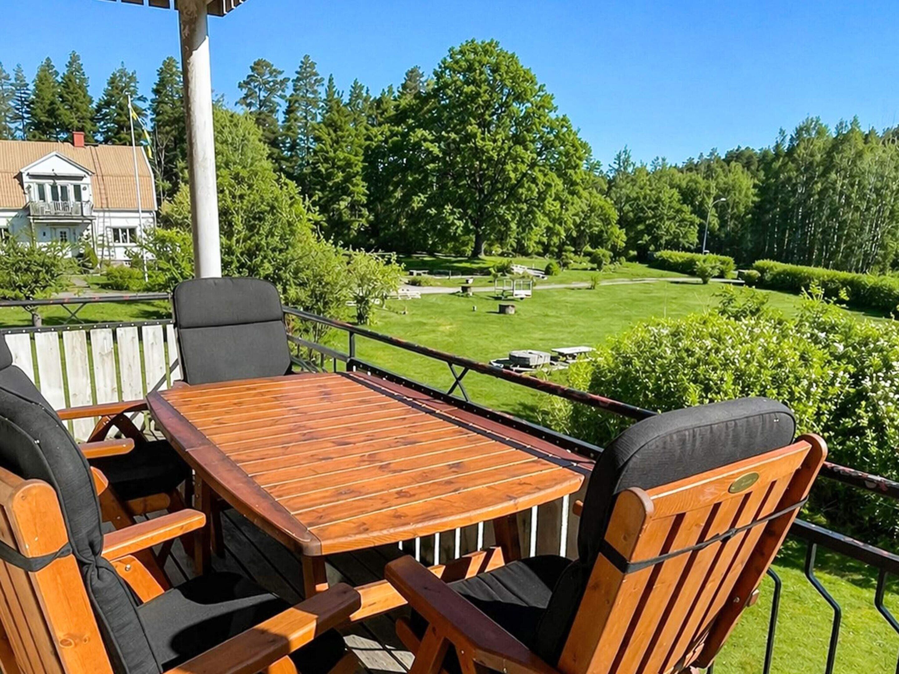 A wooden deck with a table and chairs, overlooking a well-maintained lawn and trees.