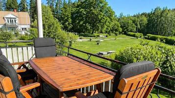 A wooden deck with a table and chairs, overlooking a well-maintained lawn and trees.