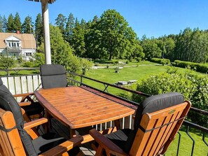 En träveranda med ett bord och stolar, med utsikt över en välskött gräsmatta och träd.