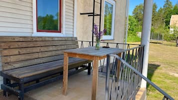 A wooden bench and table on a porch with a railing, a window, and a door.