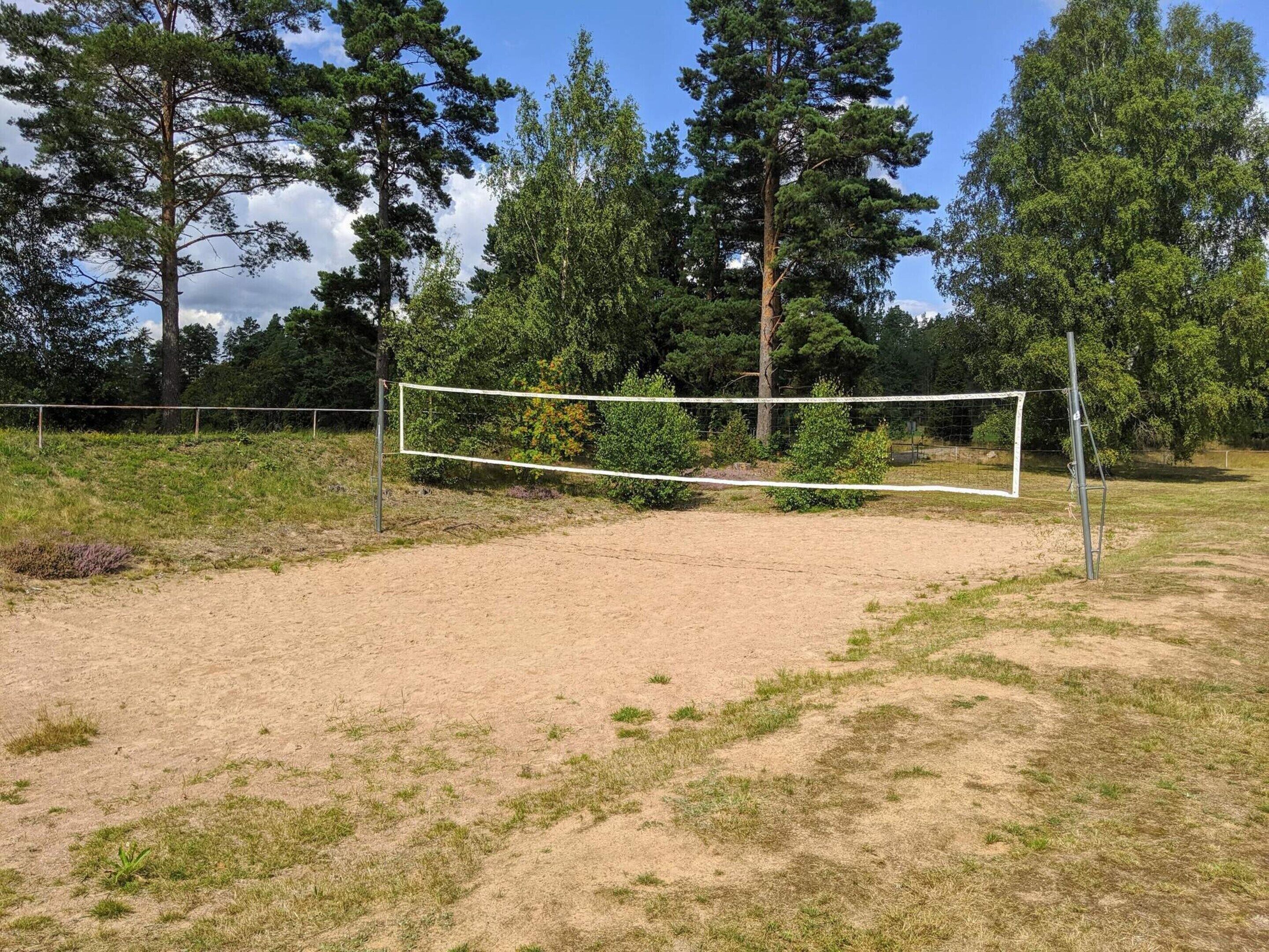 A volleyball court with a net, surrounded by trees and a grassy area.