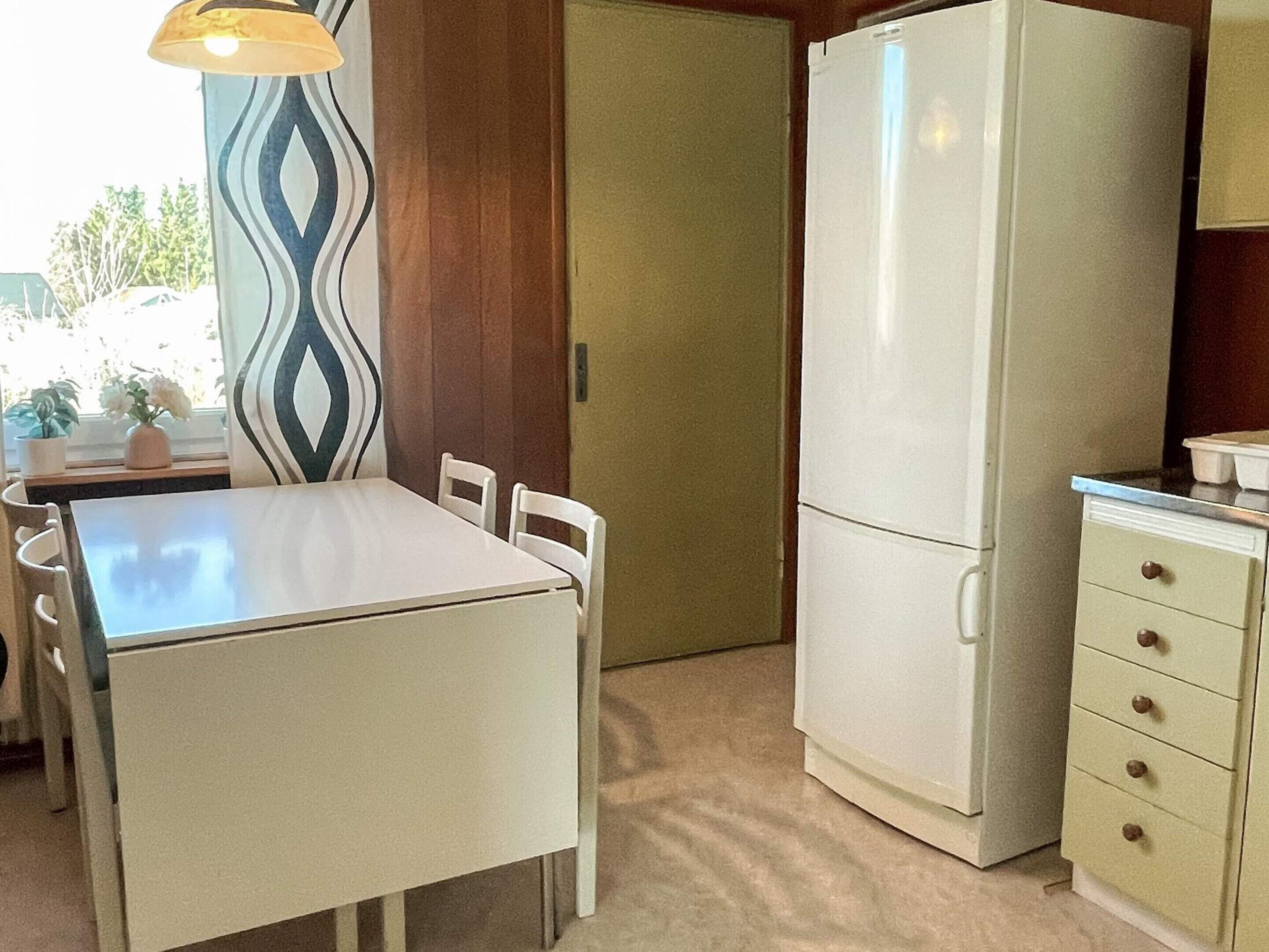 A compact kitchen with a white table, chairs, a refrigerator, and a small cabinet.
