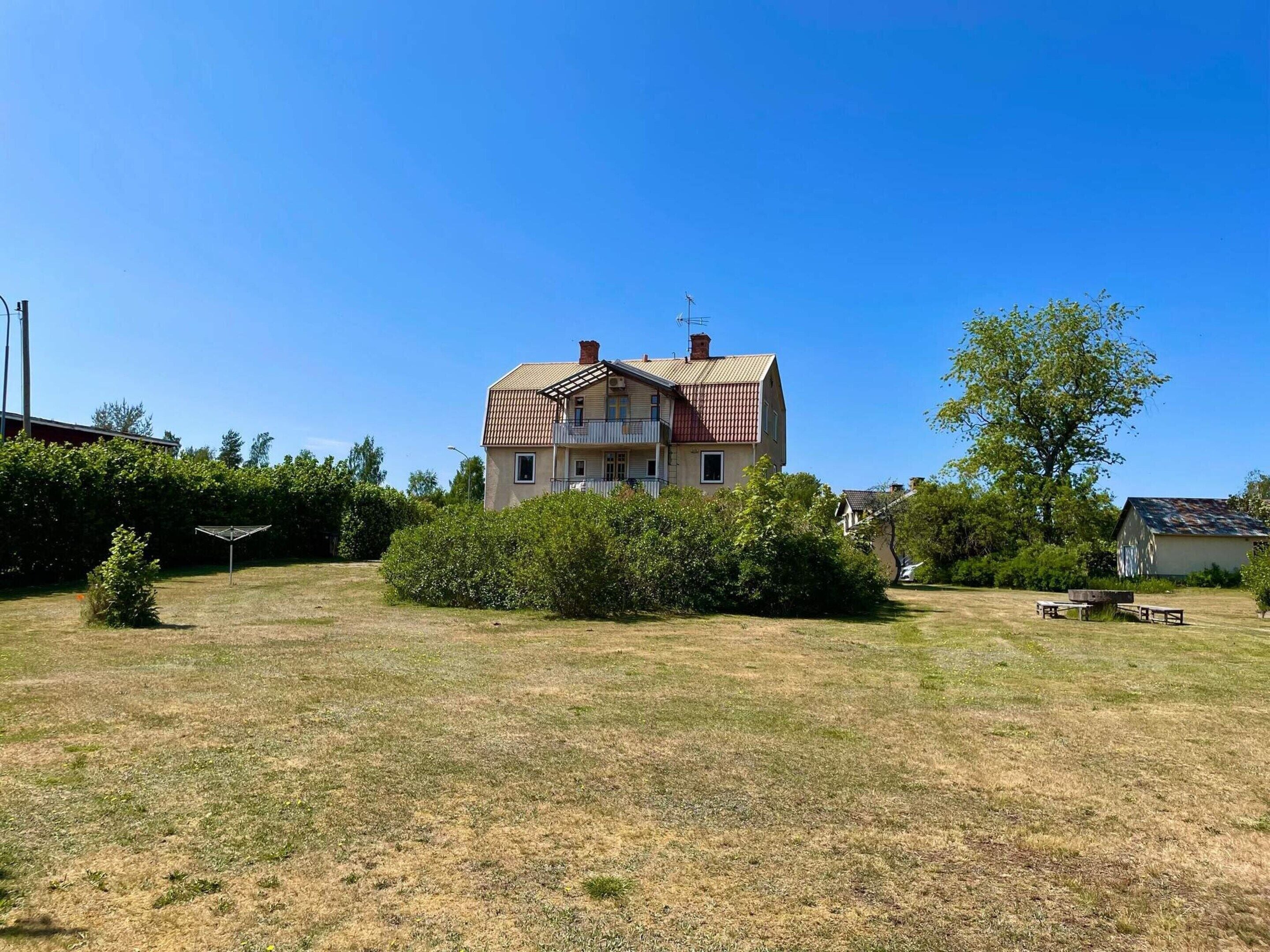 A two-story house with a sloped roof, surrounded by a grassy yard and a small tree.