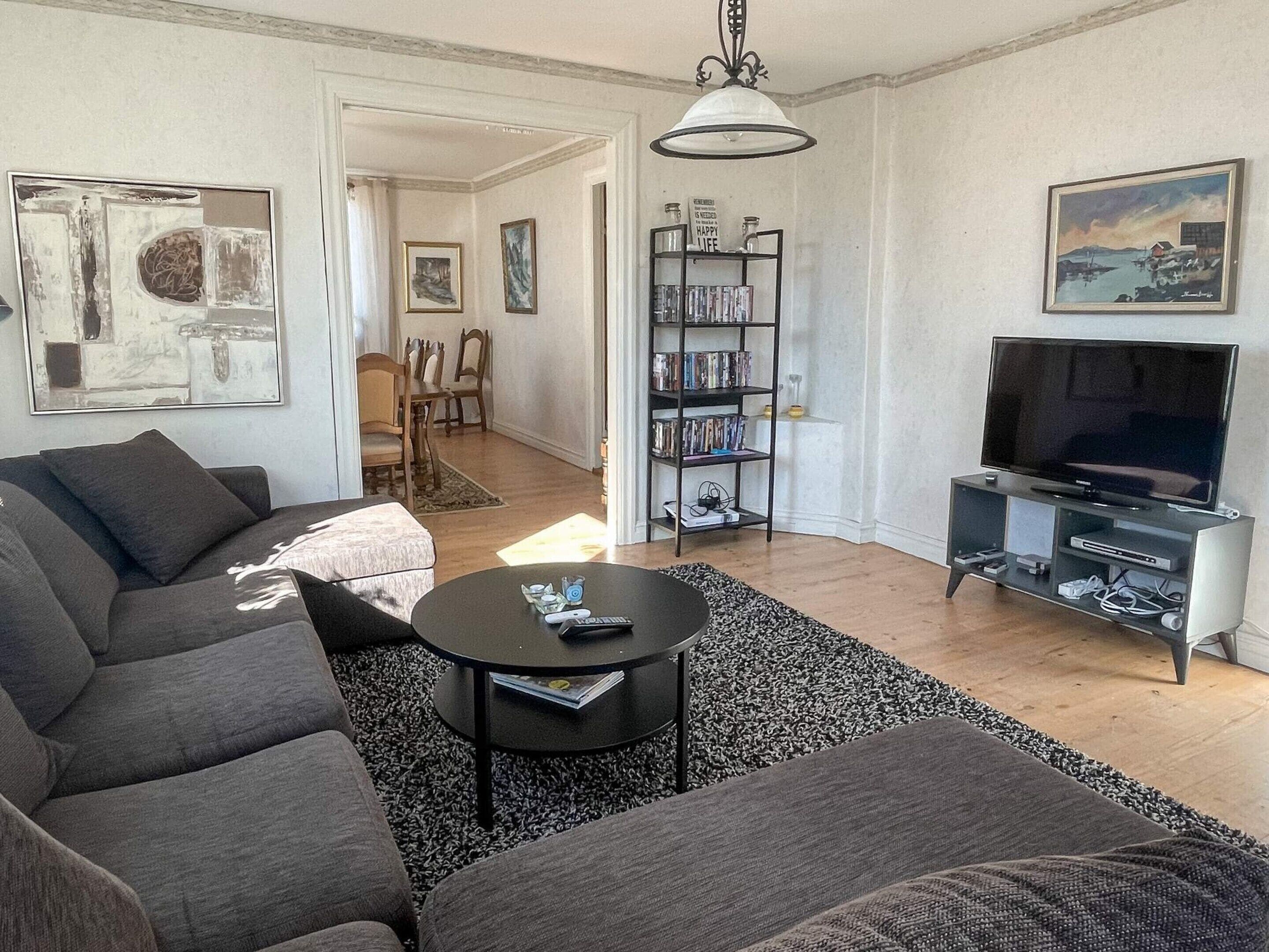 A living room with a sofa, a coffee table, a bookshelf, a TV, and a painting on the wall.