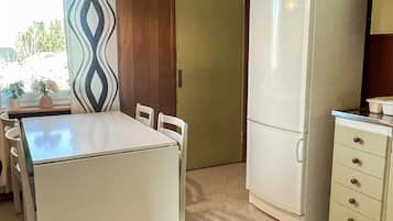 A compact kitchen with a white refrigerator, a small cabinet, and a dining table with chairs.