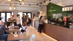 A modern cafe interior with wooden tables, white chairs, and a green wall with 'Ice-Cream & Candy' signage. - Beautiful Glamping Tent With Pellet Stove (Winterswijk - Brinkheurne)