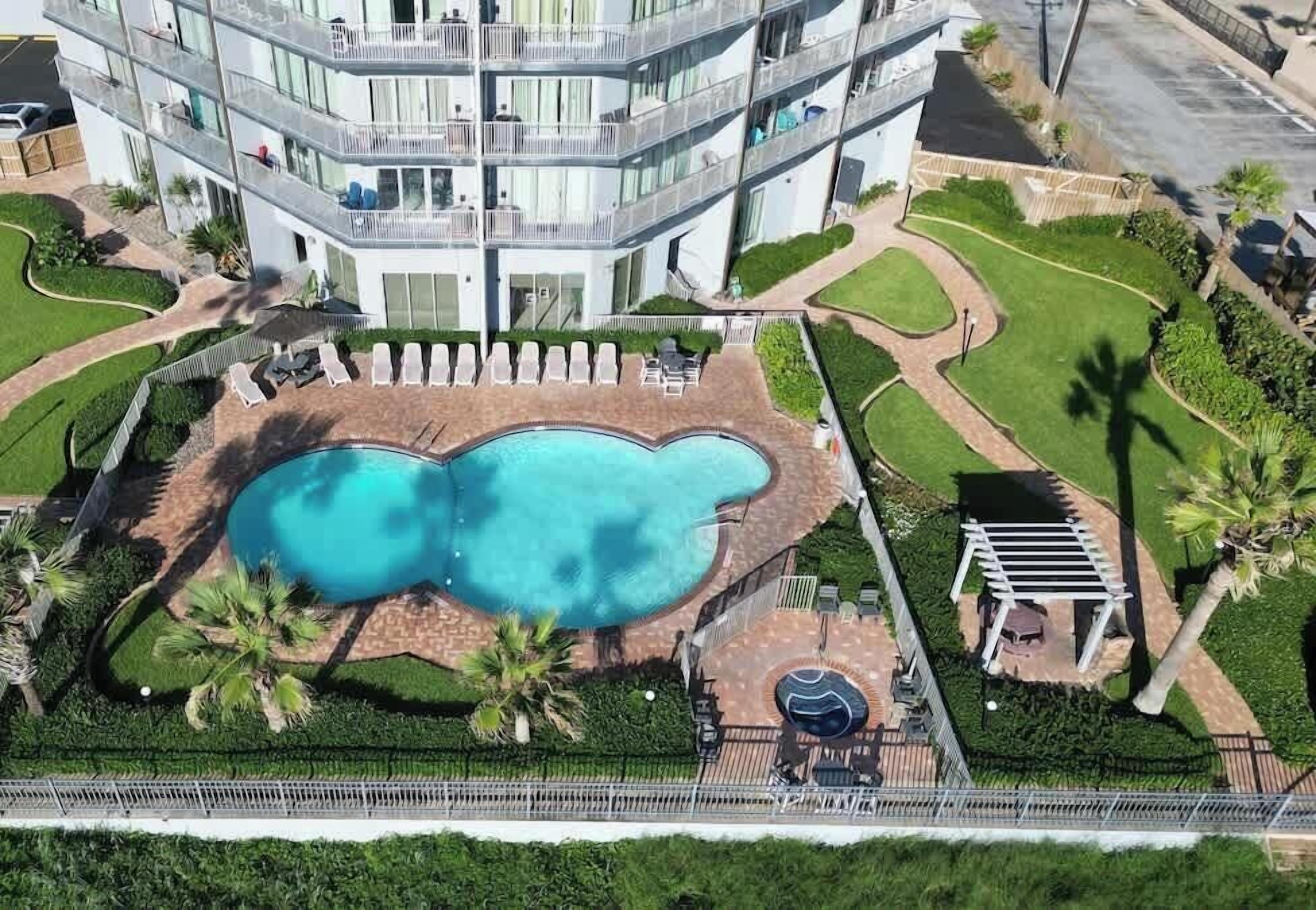 Um hotel com vários andares e uma piscina central, rodeada por relvados bem cuidados e palmeiras.