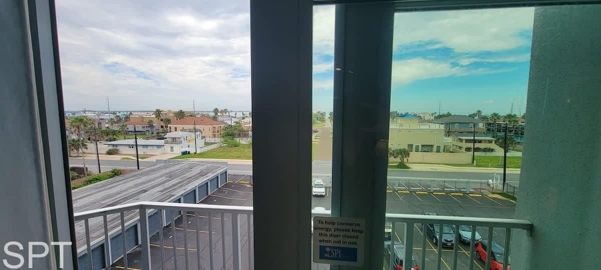 A view from a window overlooking a parking lot and buildings, with a sign indicating the door is closed when not in use.