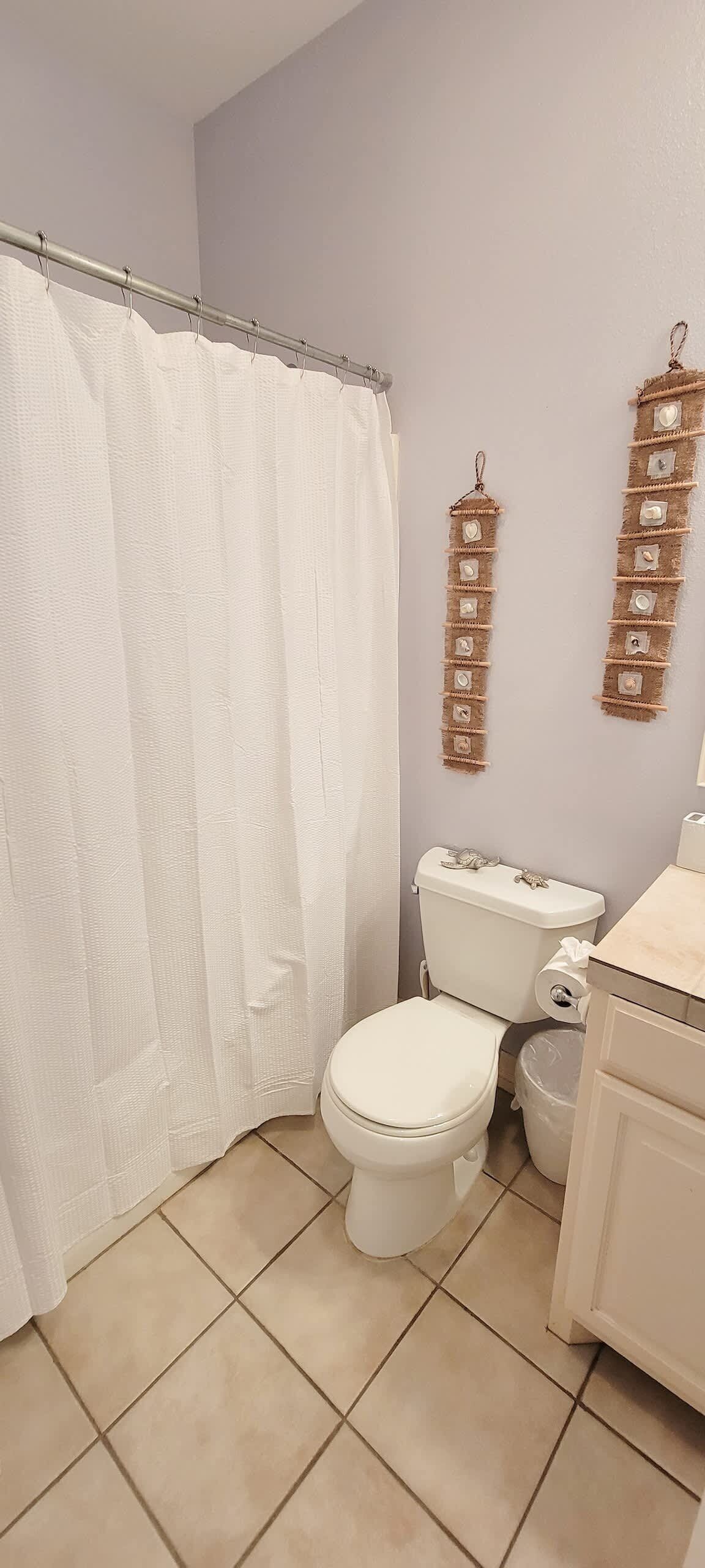 A bathroom with a white toilet, a shower curtain, and a sink with a beige countertop.
