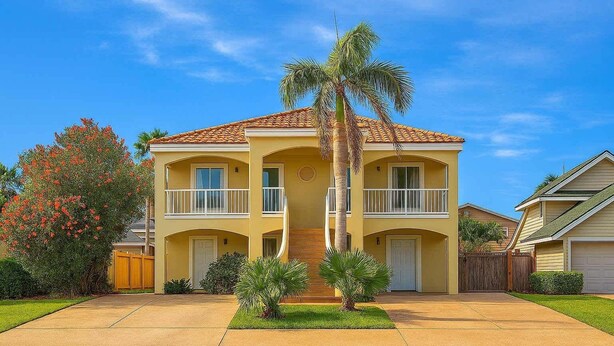 A two-story residential building with a central entrance, a covered front porch, and a two-car garage. - Beach & Palms Condo 2 Bedroom Condo by RedAwning (South Padre Island)