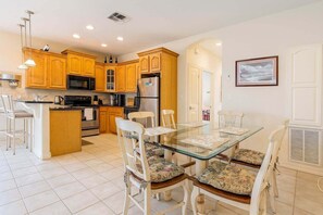 A modern kitchen with wooden cabinets, a central island, and a dining area with a glass table and white chairs. - Beach & Palms Condo 2 Bedroom Condo by RedAwning (South Padre Island)