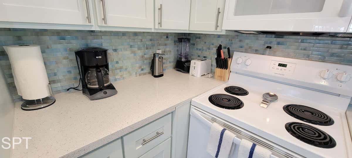 A kitchen with white cabinets, a coffee maker, a toaster, and a stove.