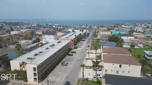A coastal urban area with a mix of residential and commercial buildings, a parking lot, and a view of the ocean.