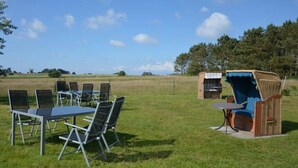 An outdoor seating area with a table and chairs, a wicker chair, and a small structure in the background. - 3 in Haus Pax Modern Retreat (Nebel)