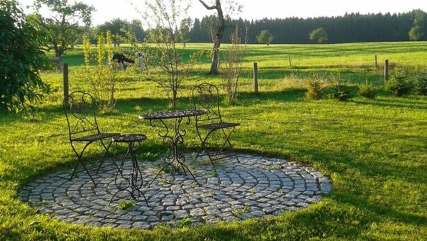 A circular stone patio with metal chairs and a table, surrounded by a grassy field and trees. - Apartment in Hergensweiler (Hergensweiler)