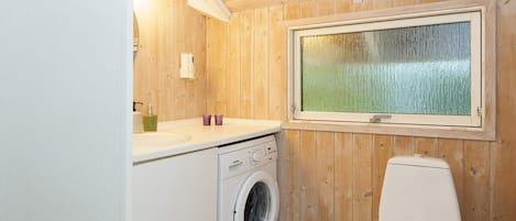A compact bathroom with a washing machine, toilet, and a window with a view.