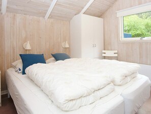 Un dormitorio con cama, dos lámparas de pared, un armario y una ventana con vistas a vegetación.