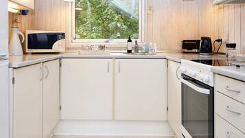 Una cocina moderna con armarios blancos, microondas, estufa y ventana con vista a follaje.