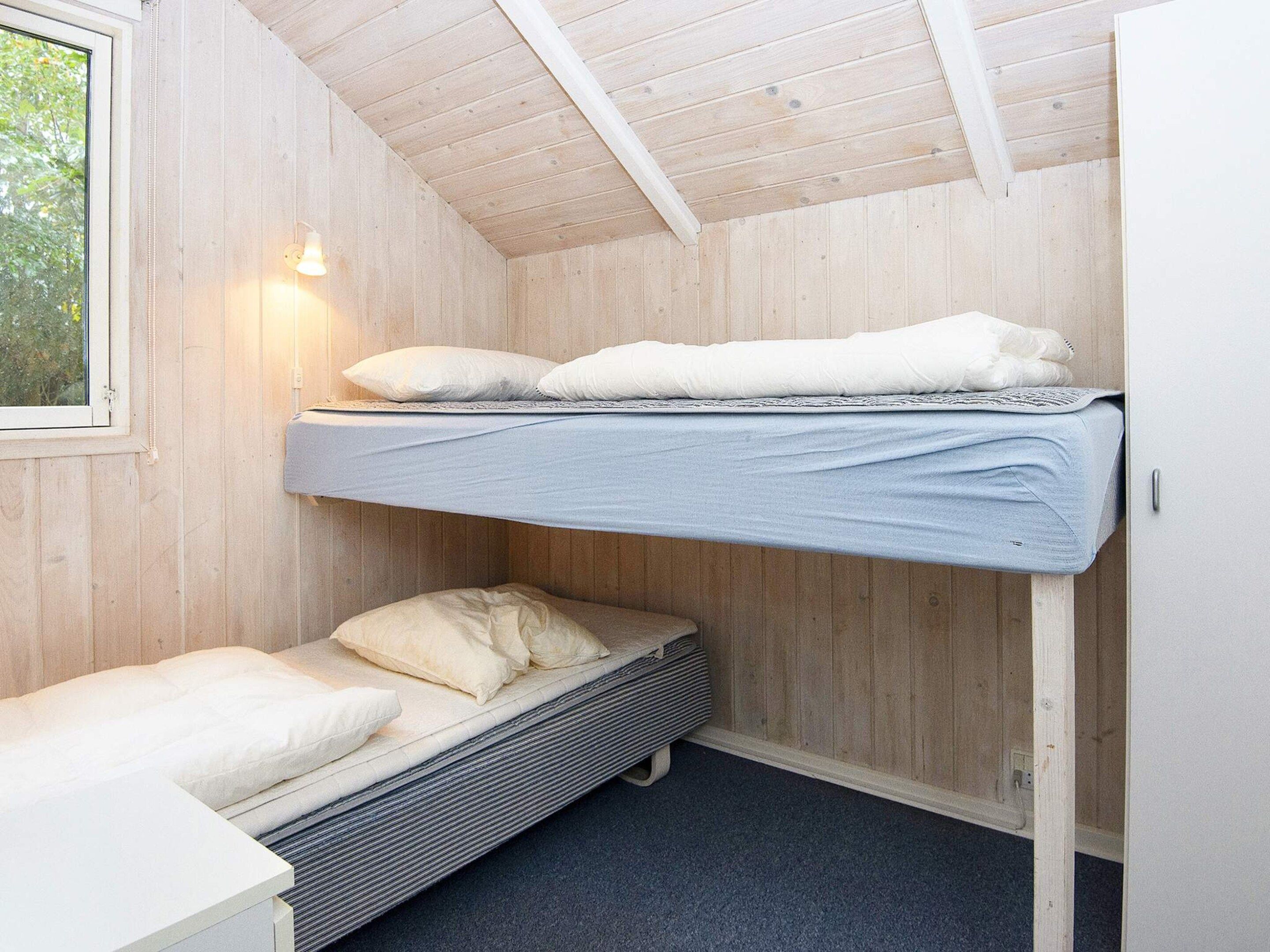A bunk bed room with a window, a wall-mounted light, and a small table.