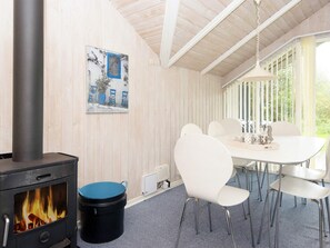 A room with a wood-burning stove, a dining table with chairs, and a window with vertical blinds. - 6 Person Holiday Home in Farvang (Farvang)