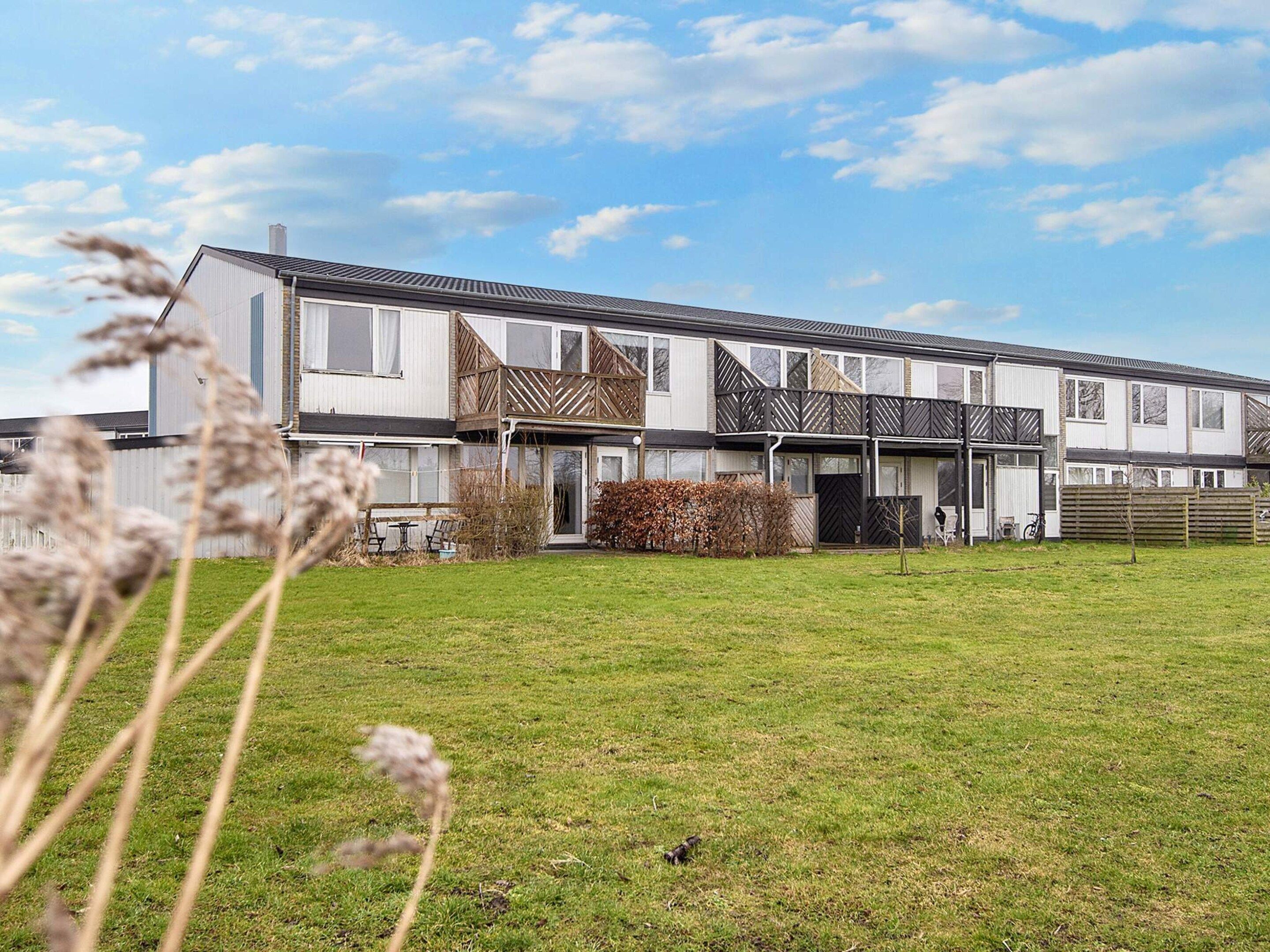 A modern multi-story residential building with a flat roof, large windows, and a well-maintained lawn in the foreground.