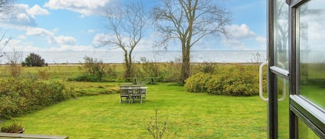 A deck with a table and chairs, overlooking a grassy yard with a view of the sea.