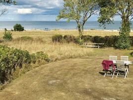 Zona verde con una mesa de picnic y sillas, un sendero que lleva a una playa y vista al mar.