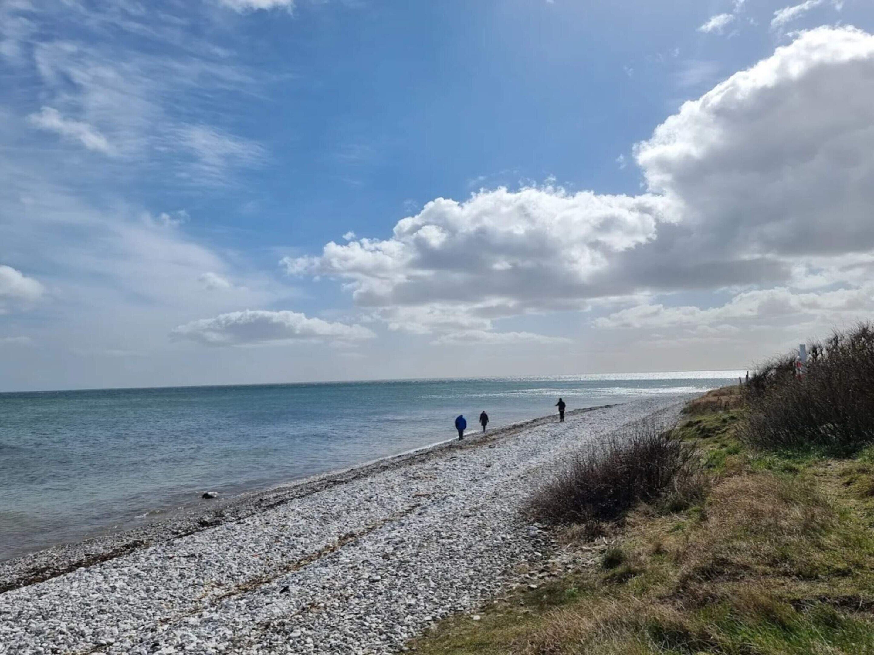 En sti med småsten der fører ned til havet, med klar himmel og enkelte skyer.