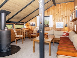 L’intérieur chaleureux d’un chalet, avec un décor en bois, un canapé, une table, des chaises, une cheminée et une fenêtre donnant sur un paysage verdoyant.