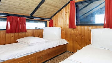 Una cabaña con dos camas, paredes de madera, una ventana con cortinas rojas y un techo con vigas a la vista.