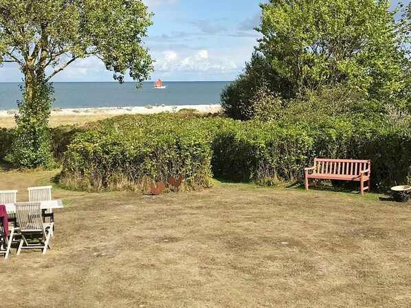A grassy outdoor area with a bench, chairs, and a view of the sea with a sailboat. - 6 Person Holiday Home in Grenaa (Grenaa)