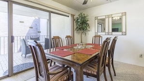 A dining area with a wooden table, red placemats, and six chairs. There is a ceiling fan, a potted plant, and a mirror on the wall. - Padre Oasis #302 2 Bedroom Home by RedAwning (South Padre Island)
