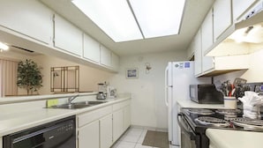 A compact kitchen with white cabinets, a dishwasher, a stove, and a microwave. - Padre Oasis #302 2 Bedroom Home by RedAwning (South Padre Island)