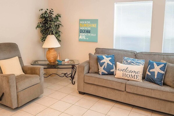 A living room with a grey sofa, a matching armchair, a glass coffee table, a floor lamp, and a wall with a motivational quote. - Sea Dancer #1 1 Bedroom Condo by RedAwning (South Padre Island)