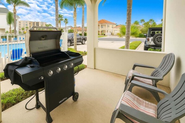 Una griglia per barbecue con quattro comandi, una superficie grill coperta e il logo Neaghill. Sono presenti due sedie con cuscini a righe.